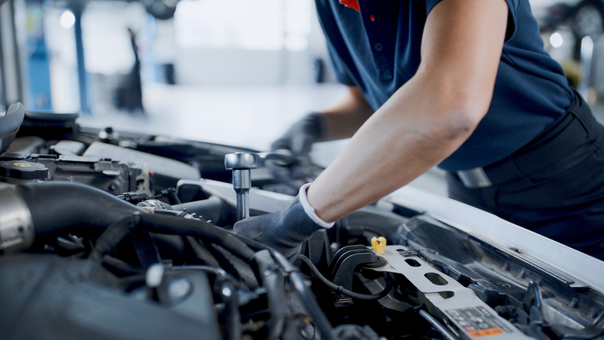 Hände einer Mechanikerin, die in der Werkstatt am Automotor arbeitet